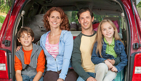 Happy family smiling behind the car